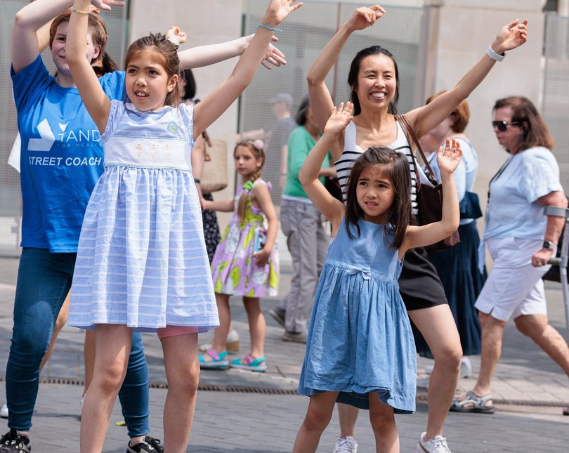 Children dressed in blue hold their hands in the air as part of an activity outdoors